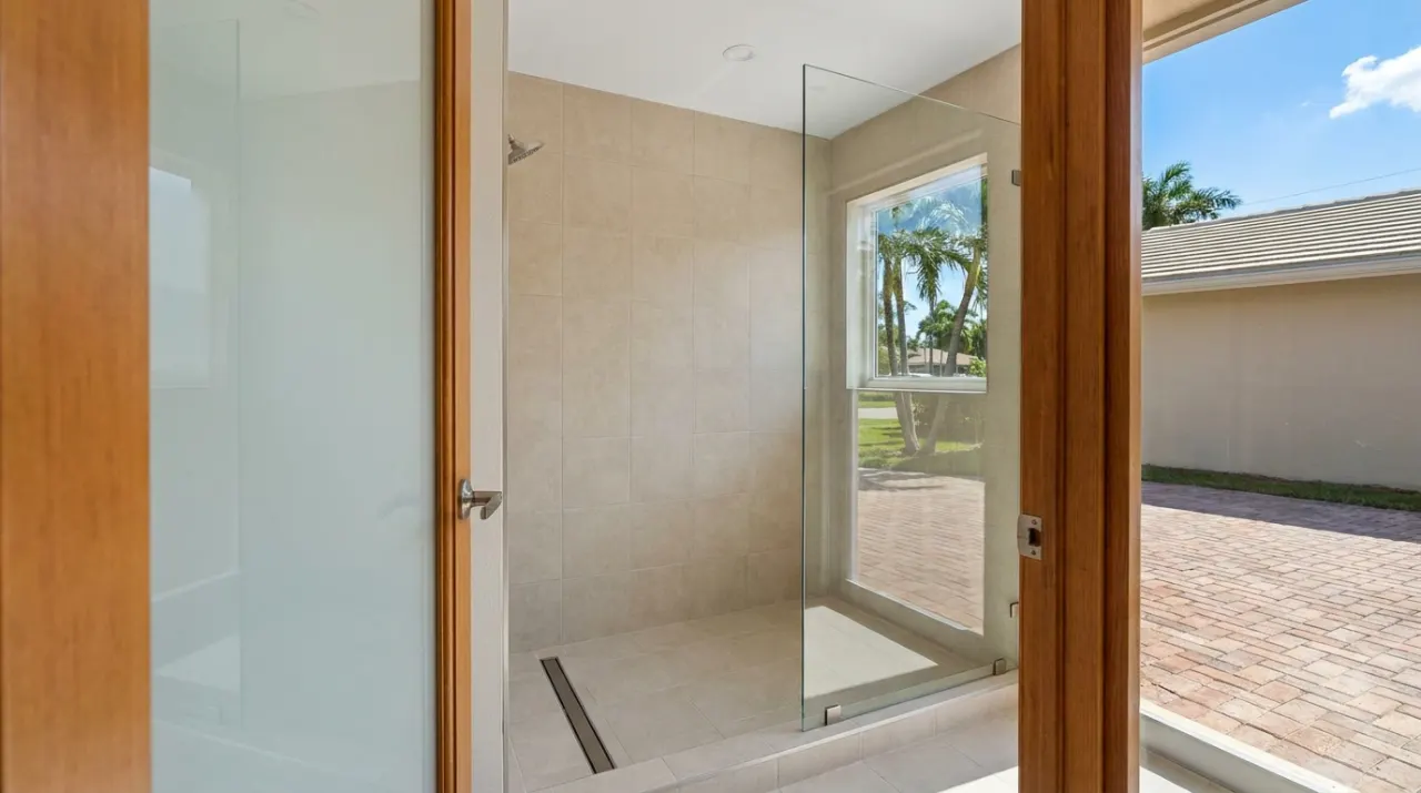 A newly tiled walk-in shower with a linear floor drain and a frameless glass panel.