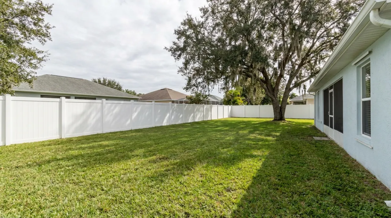 A long white vinyl privacy fence running along a wide backyard.